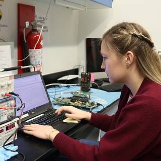 Photo of Postbaccalaureate researcher Isabella Brewer at a computer connected to electronics hardware