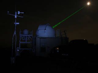 Photo of a NASA’s Goddard Space Flight Center Laser Ranging Facility directing a laser (green beam) toward the Lunar Reconnaissance Orbiter (LRO) spacecraft in orbit around the moon (white disk). 